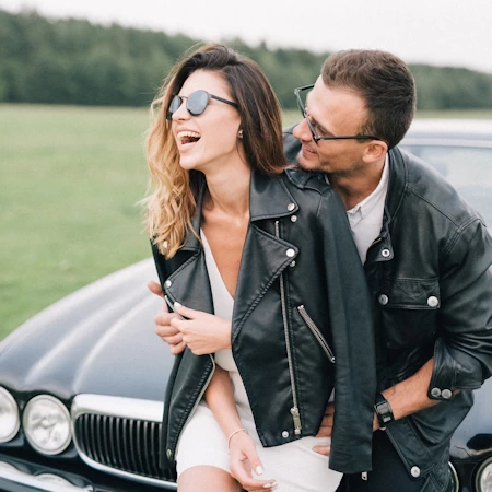 Smiling Couple sitting on car bonnet